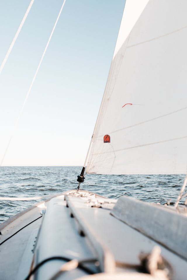 Dynamic front-view of a sailboat's bow cutting decisively through the water, representing the strategic momentum and influential presence students learn to build in the ONYX Influence Playbook.